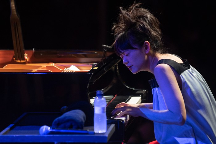 Une femme vêtue d'une robe ample grise se penche en avant sur le clavier d'un piano pendant qu'elle joue